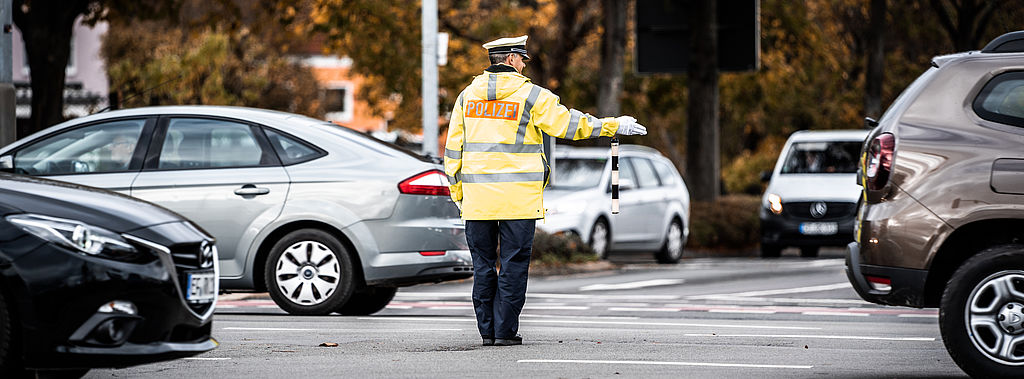 Polizist regelt auf befahrener Straßenkreuzung den Verkehr.