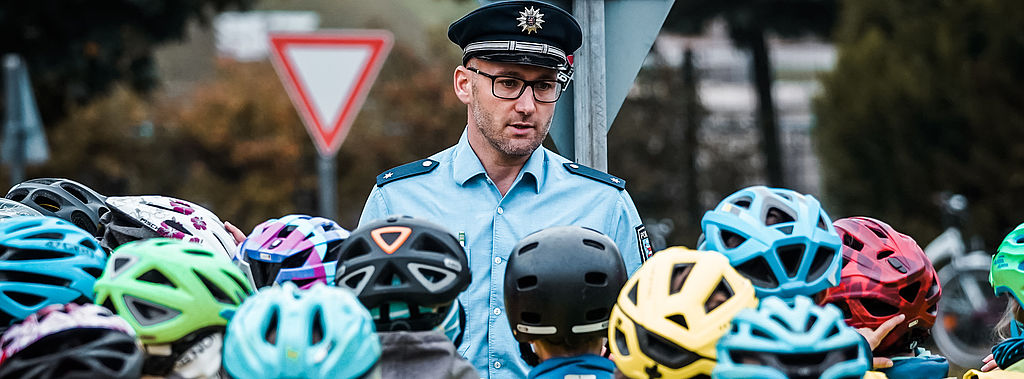 Polizist erklärt Kindern die Regeln für den Fahrradverkehr. Link: Informationen und Maßnahmen zur Vorbeugung von Kriminalität und Straftaten