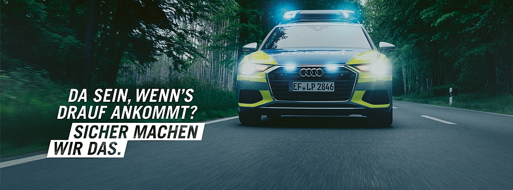 Polizeifahrzeug fährt mit Blaulicht auf einer Straße im Wald; Text: Da sein, wenns drauf ankommt? Sicher machen wir das.