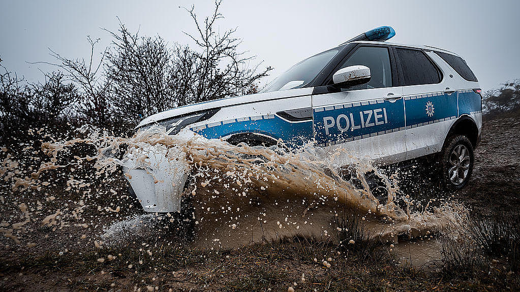 Polizeiauto fährt durch eine große, schlammige Pfütze.