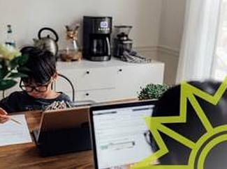 Junge mit Brille vor einem Computer und schreibt mit einem Bleistift auf ein weißes Blatt Papier.