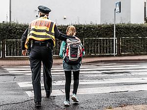 Eine Polizistin führt ein Mädchen über einen Zebrastreifen einer Straße.