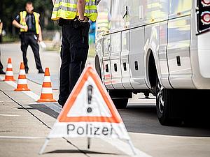 Ein Warndreieck der Polizei vor einem Bus, welcher von Polizisten in Warnweste kontrolliert wird.