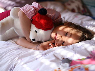 Kleines Mädchen liegt im Bett mit ihrem weißen Teddy im Arm.