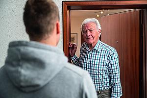 Bild zeigt einen älteren Herren im Gespräch mit einem jüngeren Mann an der Hauseingangstür