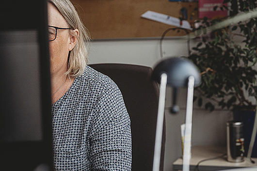 Sachbereichsleiterin für Systemintegration an ihrem Arbeitsplatz. Sie ist von vorn zu sehen mit Blick auf den Bildschirm. Ihr Gesicht wird vom Bildschirm verdeckt
