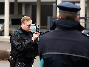 Ein Polizist schaut durch ein Lasermessgerät. Ein zweiter Polizist schaut zu.