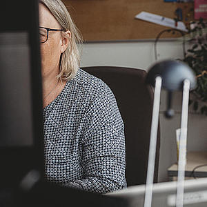Sachbereichsleiterin für Systemintegration an ihrem Arbeitsplatz. Sie ist von vorn zu sehen mit Blick auf den Bildschirm. Ihr Gesicht wird vom Bildschirm verdeckt