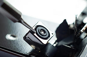 A bug for tracking and recording videos. The micro camera is hidden. Eine versteckte Mikrokamera wird mit einem kleinen Schraubenzieher bearbeitet.