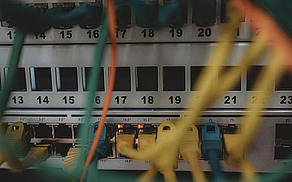 eine Detailaufnahme im Serverraum, die Kabel sind im Vordergrund, im Fokus leuchten LEDs