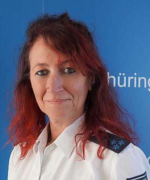 Das Bild zeigt: Eine Frau mit dunkelroten Harren. Sie trägt eine Polizeiuniform