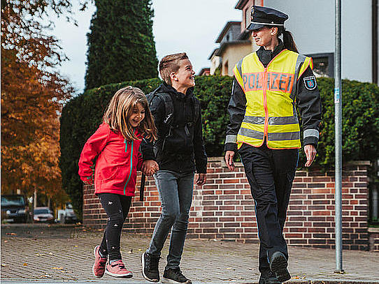 Polizeiliche Prävention für Kinder im Straßenverkehr Polizistin führt zwei Kinder über Zebrastreifen