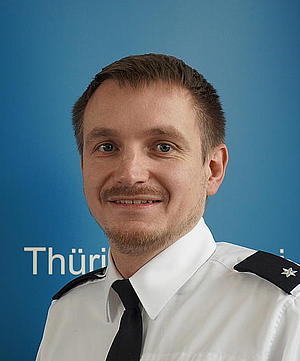 Das Bild zeigt: Einen Mann mit kurzen blonden Haaren. Er trägt eine Polizeiuniform