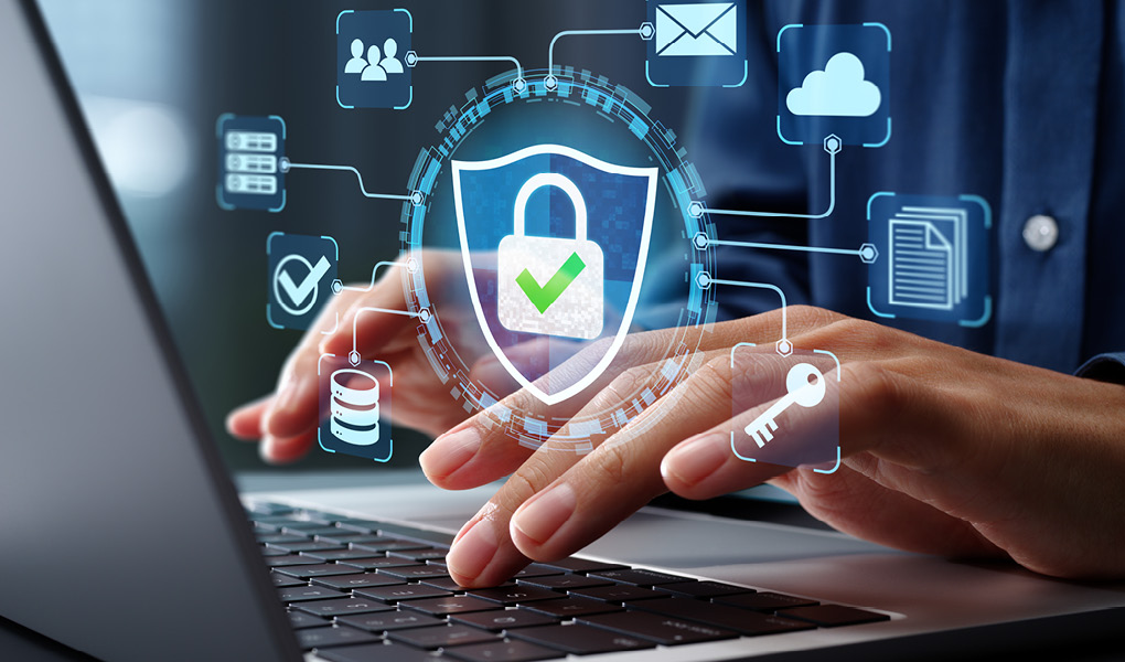 Ein Laptop von der Schrägseite. 2 Hände tippen auf der Tastatur. Über dem Laptop sind verschiedene Cyber-Security Symbole zu sehen