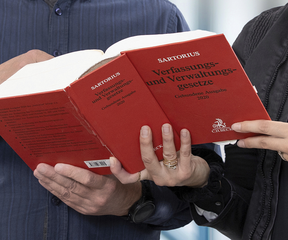 Nahaufnahme eines Gesetzbuches, welches aufgeschlagen von 2 Personen gehalten wird.